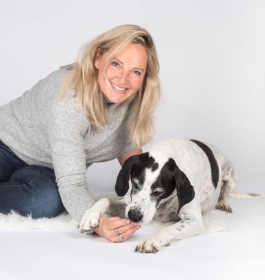 Eine lächelnde Frau sitzt neben einem Hund und streichelt ihn auf dem Boden.