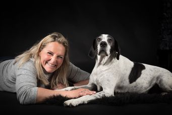 Frau mit blonden Haaren lächelt, liegend neben einem schwarzen und weißen Hund.